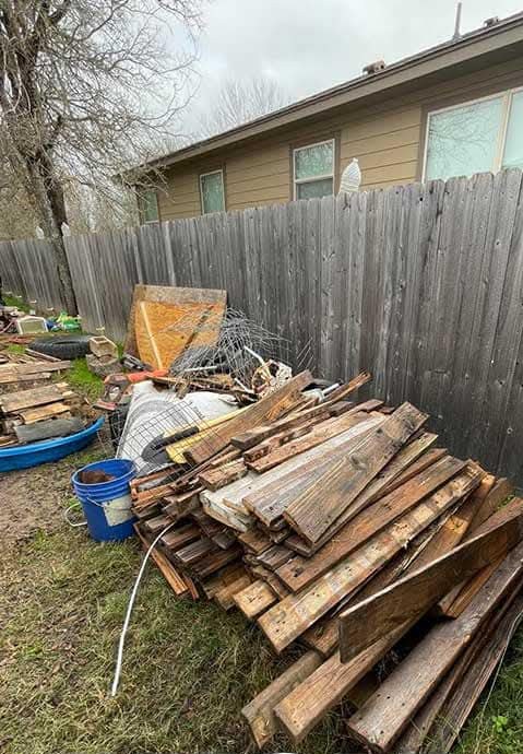 Before: pile of old lumber and junk along a fence